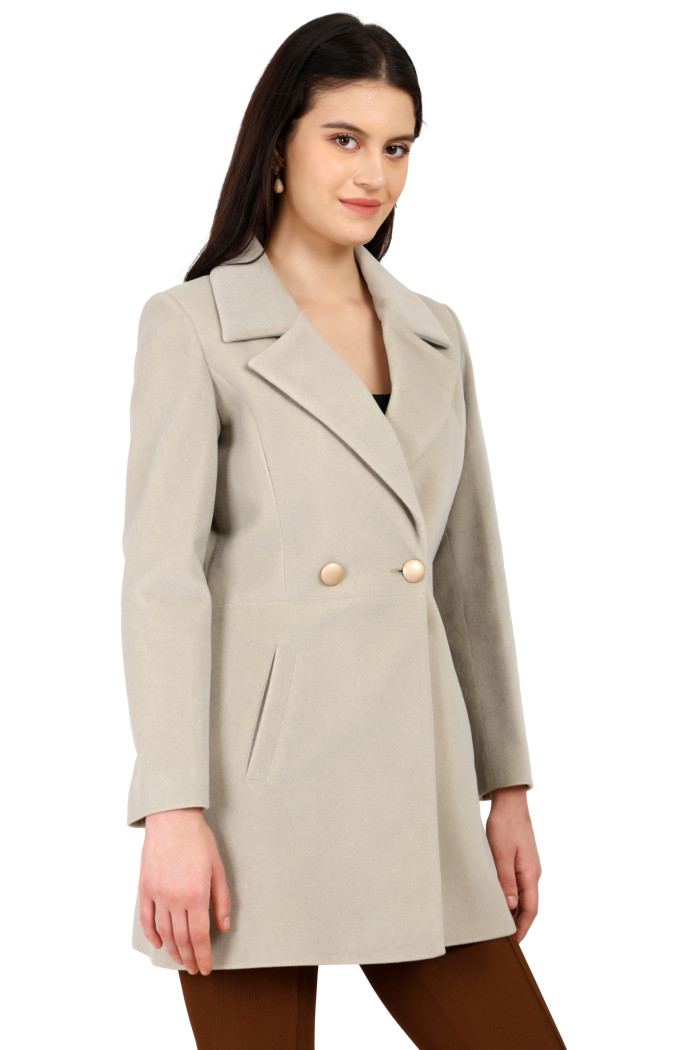 A standing side pose of a woman wearing Trufit’s double-breasted velvet coat in mint green with a lapel collar, side pockets, button closure, and brown tights.